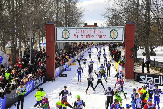 Glada skidåkare passerar mållinjen under Vasaloppets klassiska målportal.