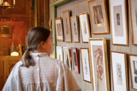 A guide at Carl Larsson-gården walking pass a wall full of paintings.