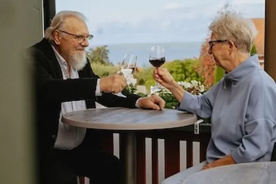 Older couple on the balcony with a glass of wine.