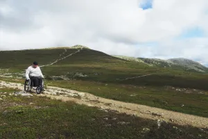 En man i rullstol tar sig fram längs en stig på fjället.