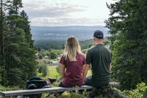 Kvinna och man sitter på en träbänk och blickar ut över utsikten.