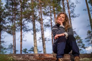 Emmy Ihlar sitter på trädstam i skogen.