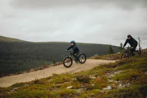 Ett barn och en vuxen cyklar i fjällmiljö.
