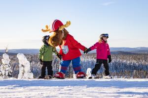 Två barn på skidor håller en person utklädd till älg i händerna.