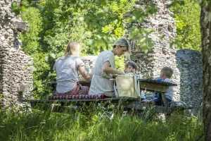 En familj äter vid ett bord utomhus bland grönska.