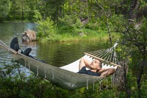 En man vilar i en hängmatta vid ett vattendrag.