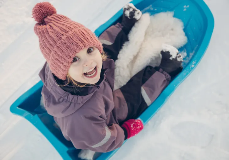 Flicka åker pulka i snön.