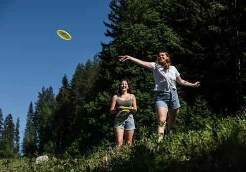 Två kvinnor spelar discgolf och kastar en frisbee.