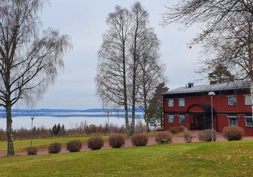 Ett rött hus bredvid kala träd och en grön gräsmatta. En stor sjö i bakgrunden.