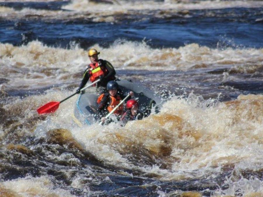 Three people in a rubber dinghy in the middle of the rapids.