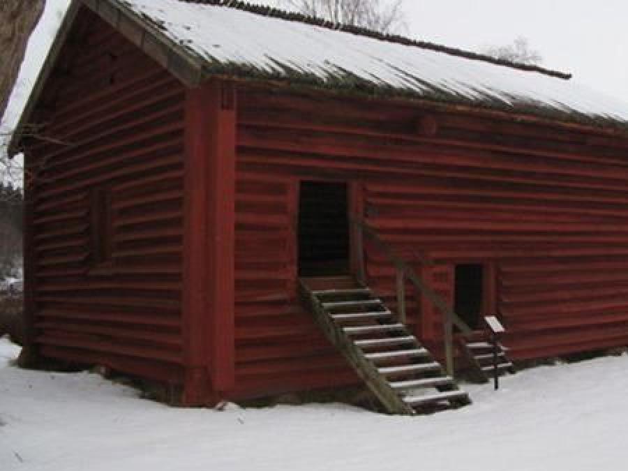 Röd äldre timmerlada, två dörrar av mindre  modell med en enkel trapp upp till dörren, vinterbild.