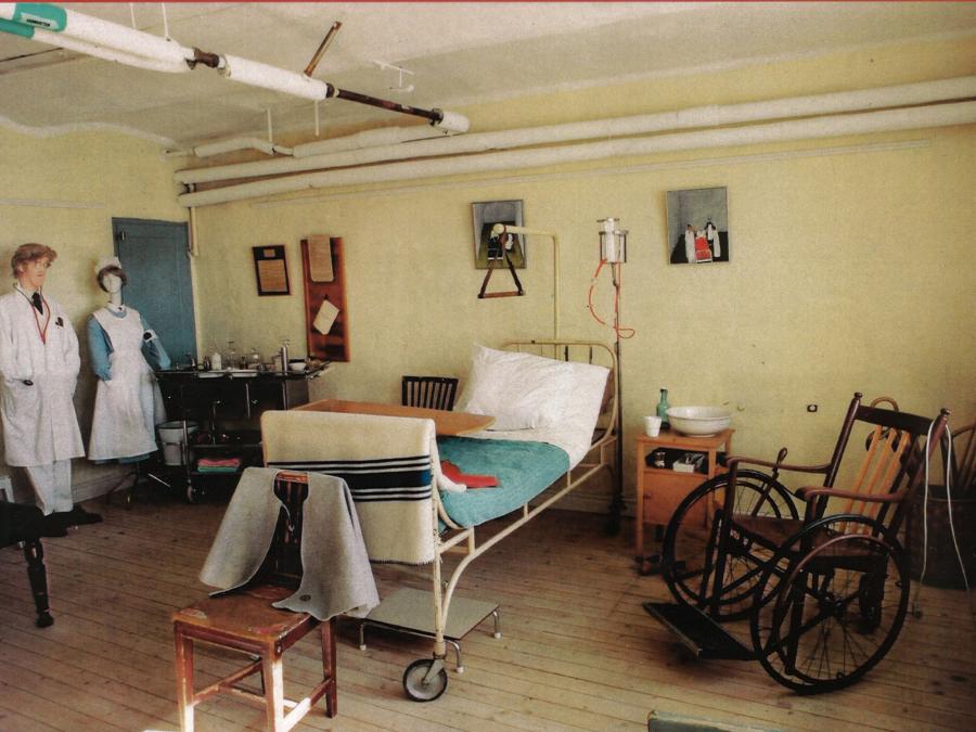Ett rum med gammeldags sjukvårdsmaterial, en säng, en rullstol, skyltdockor med sjuksköterske uniform.