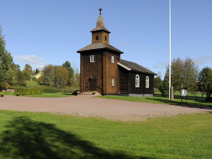 Åsens Kapell med grusplan och gräsmatta framför och flaggstång bredvid 