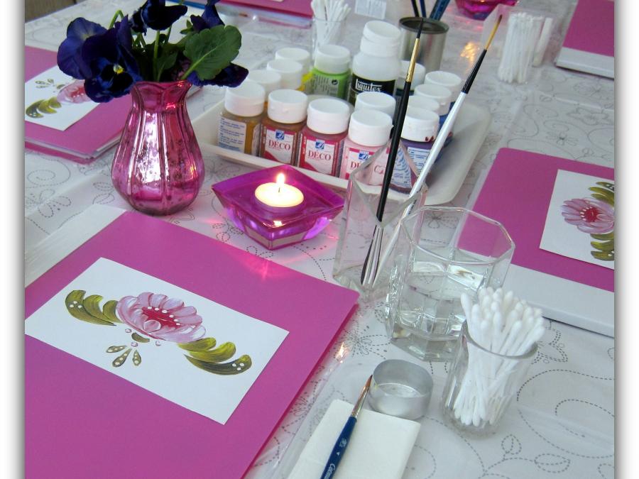 Ett bord med rosa kursmappar, färger, penslar, ljuslyktor och blommor.