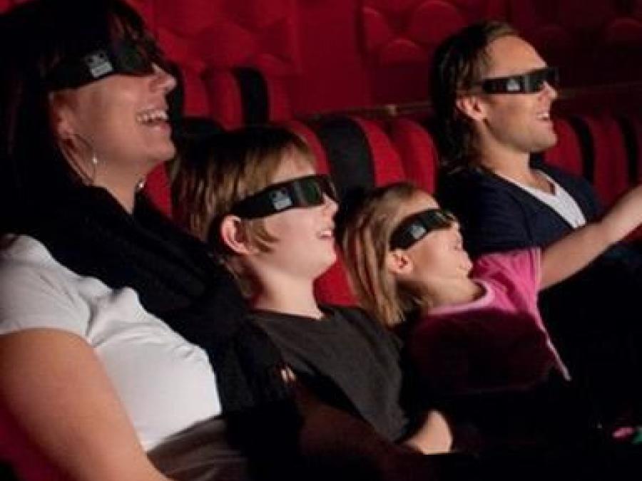Familj med två vuxna och två barn sitter med 3d glasögon i biosalongen. 