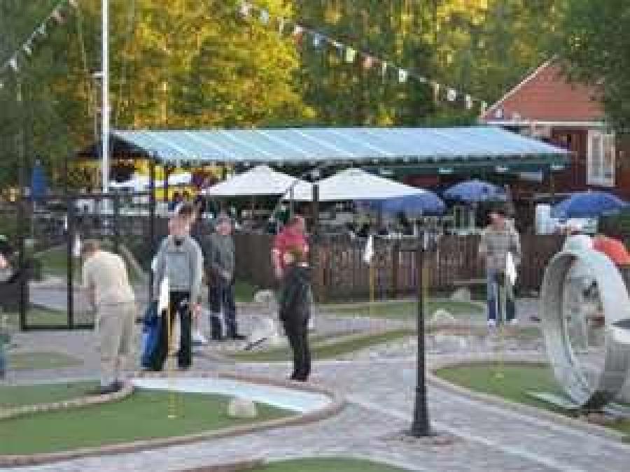 People playing miniature golf, café in the background.