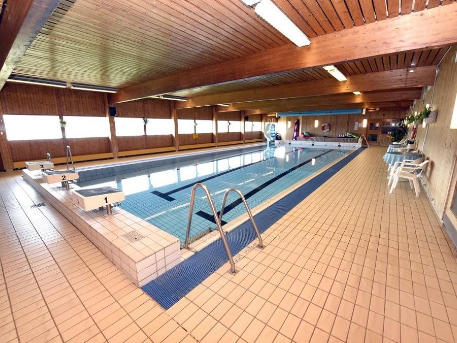 An indoor pool, a ladder at the front, white plastic chairs along the wall.