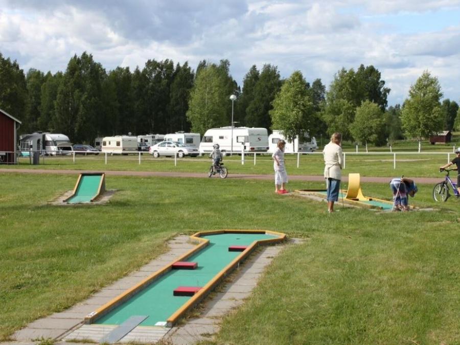 Personer som spelar på golfbanan med husvagnar i bakgrunden. 