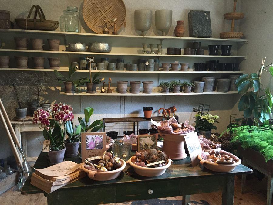 A dark wood table with flowers and various products, along the wall shelves with pots and other interior details.