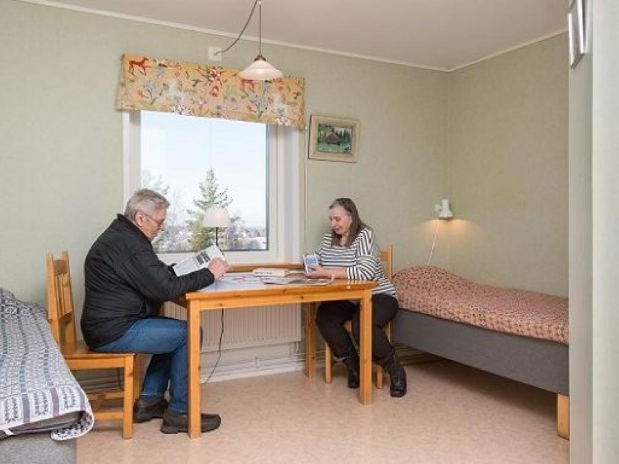 A couple are playing cards by a table in front of the window in the bedroom.