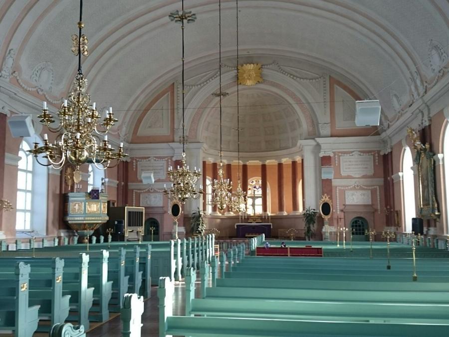 Inne i kyrkan med kyrkbänkar, ljuskronor och altare.