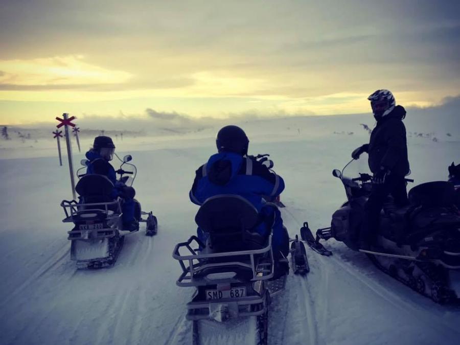 Snowmobile riders on a snowmobile trail in a mountain environment.
