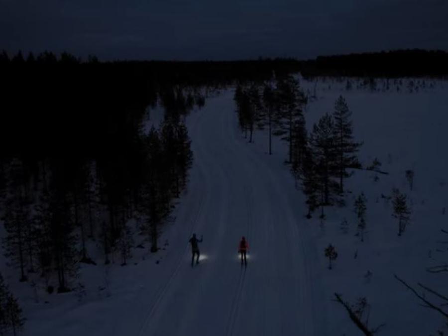 två skidåkare med pannlampor åker i spåret i mörker