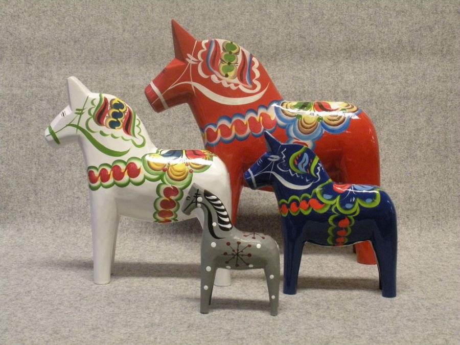 Tre dalahästar, en vit en röd, en blå i olika storlekar, en grå Faluhäst med svart och vitt mönster.