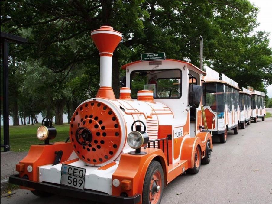 Ett orange och vitt turisttåg som åker på en gata.