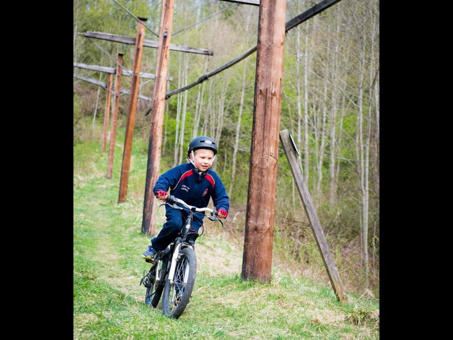 A boy cycling along a grass path, next to the path are poles on display.