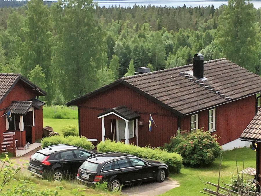 Two cars parked in front of a red cabin with black roof. 
