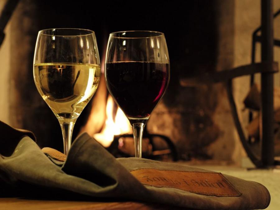 Two filled wine glasses and a fire in the background.
