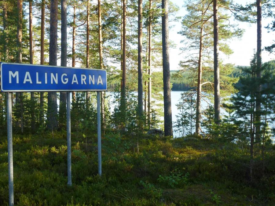 Sign with the text Malingarna on, the lake can be seen in the background between the trees.