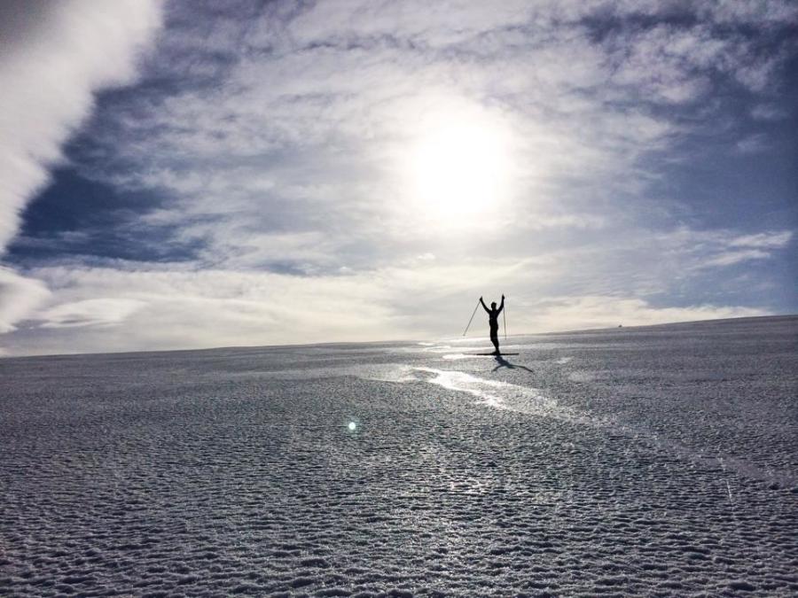 En person på skidor på vita fjällvidder sträcker armarna mot himlen. 