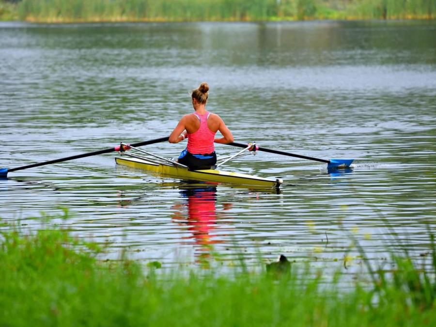 Woman is rowing in a sculler on the river. 