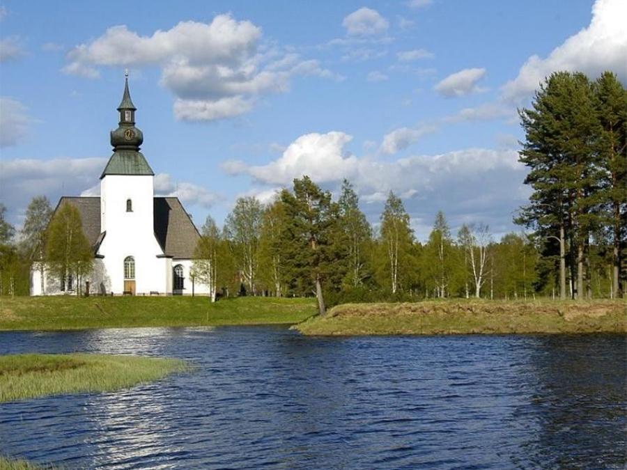 Exteriör kyrkan med vattendrag framför och grönska omkring.