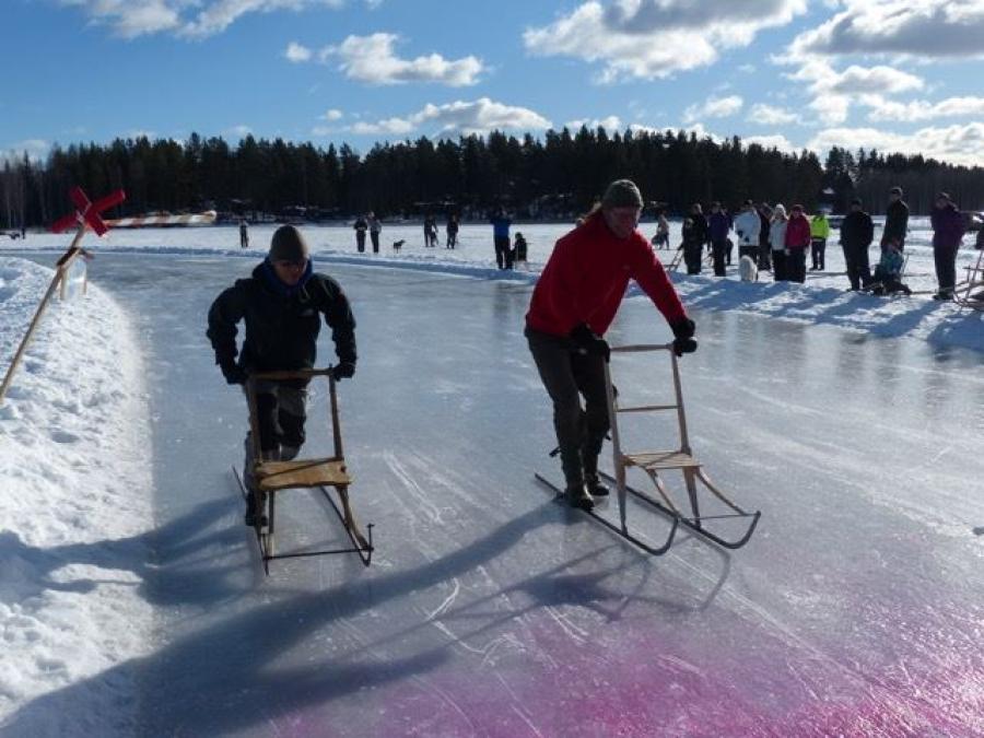 Två personer som åker på varsin spark på isen.