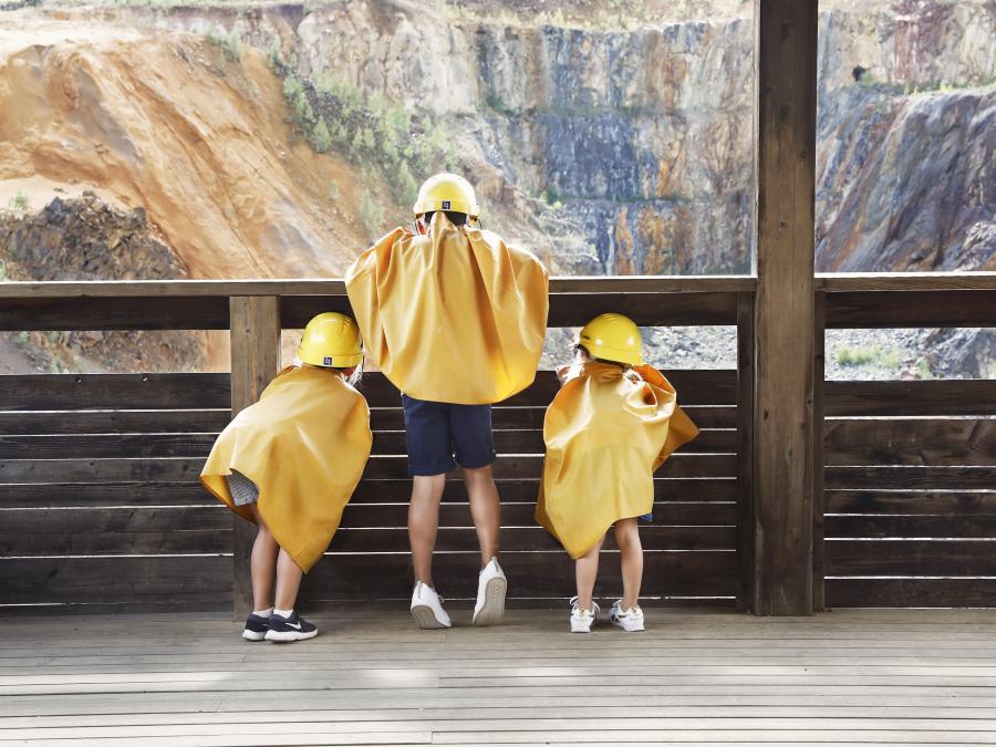 Three cjildren in yellow raincoats looking throuhg a fence down in the great pit.