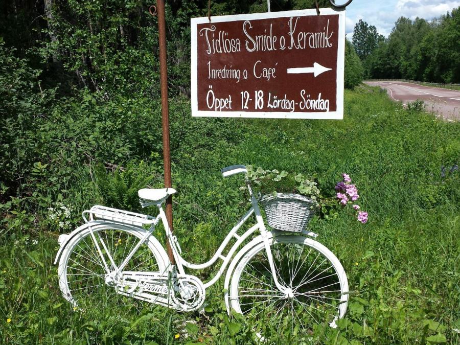 A white women's bicycle in the grass, sign Tidlösa smide & keramik.