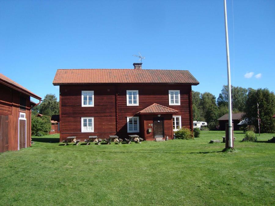 Två vånings timmerhus med gräsmatta framför och flaggstång på gården. 