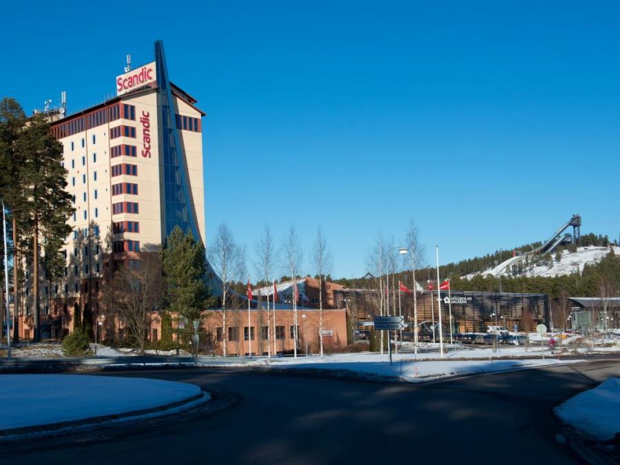 A tall bright building, red details and glass sections, ski jumps in the background.