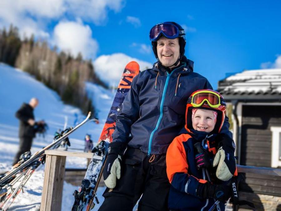 Pappa och son i skidkläder, slalombacken i bakgrunden.