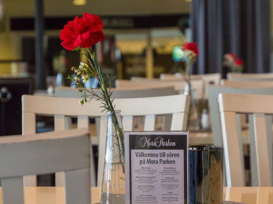 Bord med vaser med röd nejlika i och stolar på Restaurang VH i Mora Parken..
