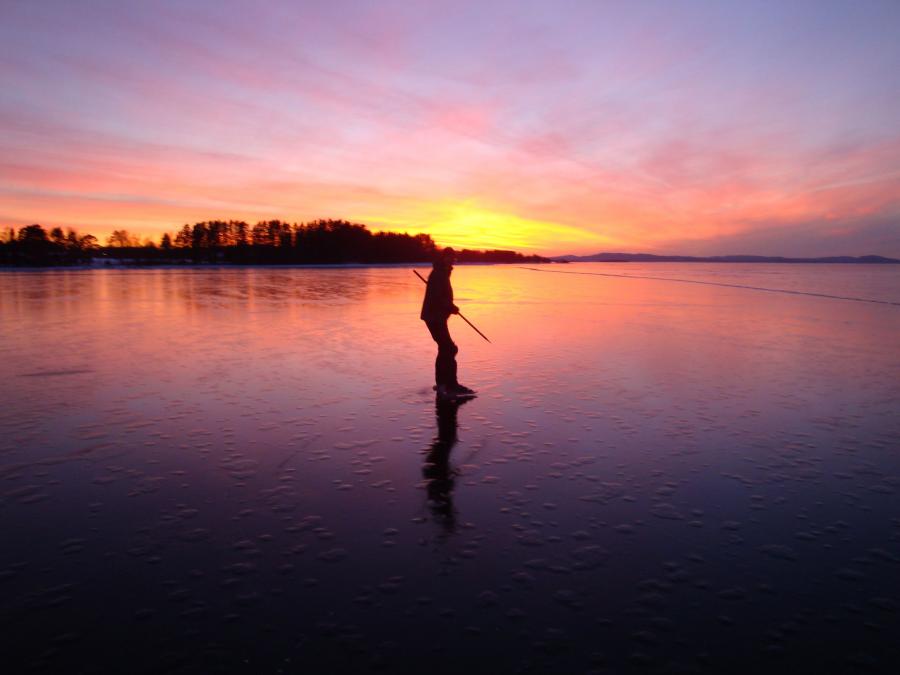 En person åker skridskor på spegelblank is i soluppgång. 