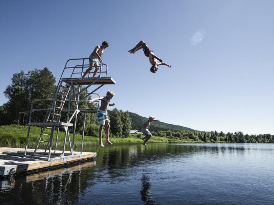 Four boys jump into the water from the trampoline.
