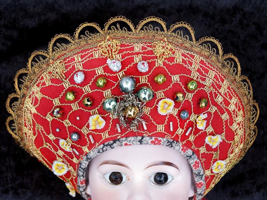 En docka som har en huvudbonad av återbruk, röd botten med guldsömmar, pärlor.