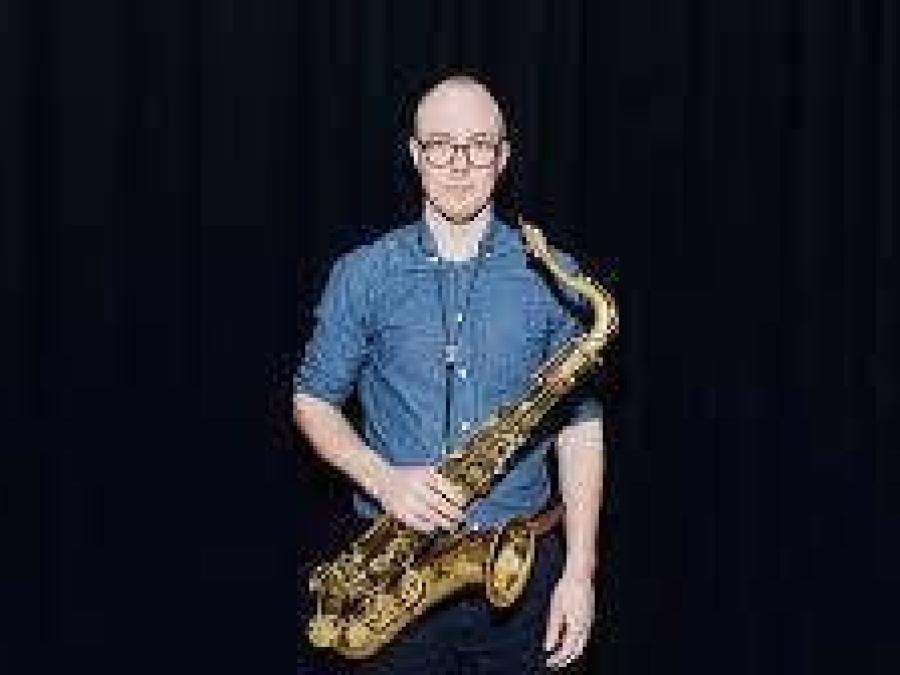 En man i blå skjorta som håller i en saxofon.