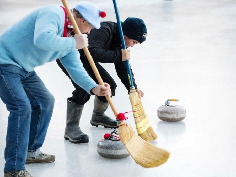 Two guys sweep with brooms on the ice.