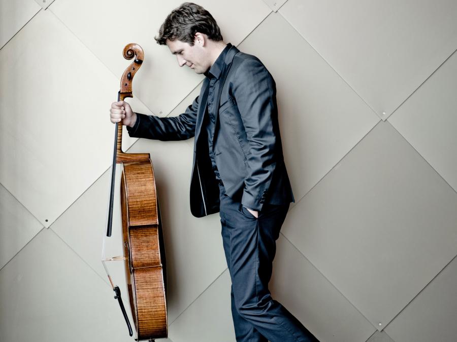 En man i blå kostym som håller i en cello med ena handen.