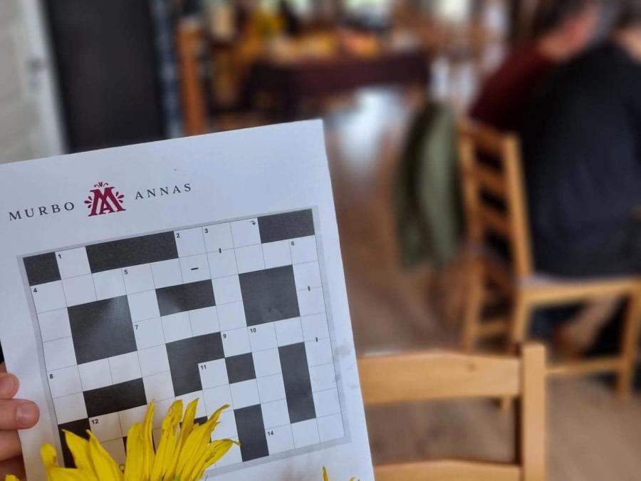 En gul blomma i förgrunden, bakom den ett kryss med Murboannas logga, i bakgrunden en restaurang med besökare.